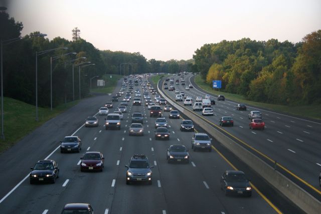 A busy highway with numerous vehicles traveling in both directions surrounded by trees.