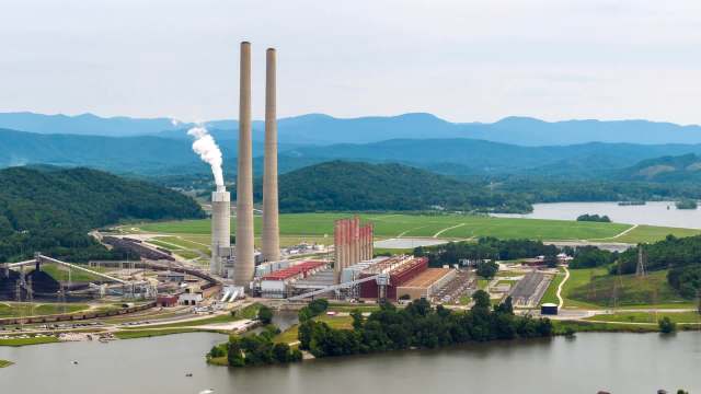 Aerial view of a coal power plant with smokestacks, surrounded by mountains and a river.