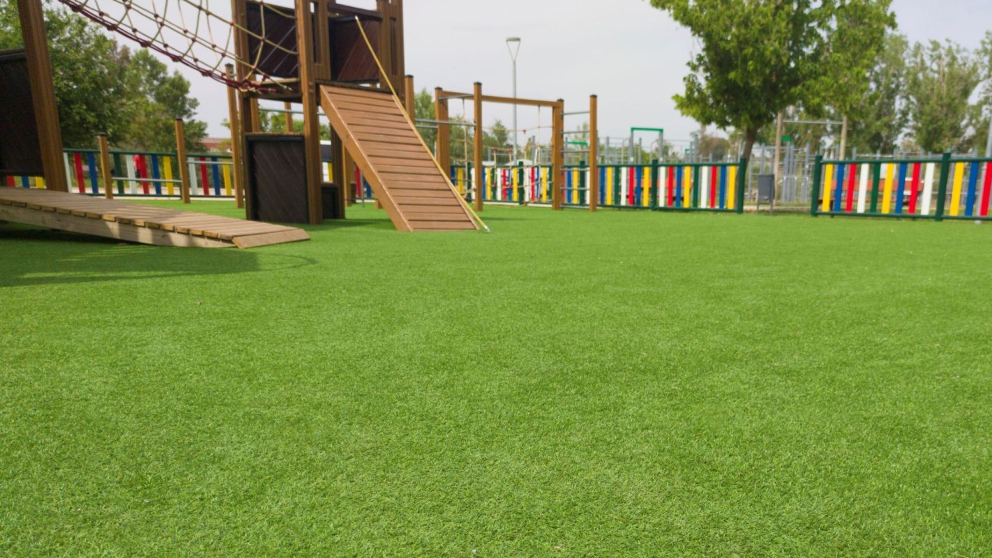 A playground with wooden structures, a ramp, and colorful fencing on synthetic turf.