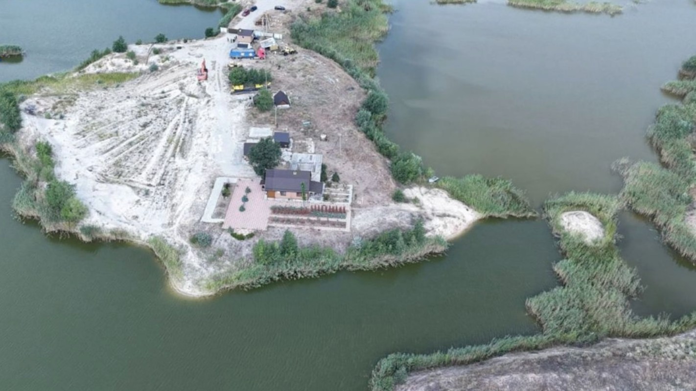 An aerial view of a riverside construction scene featuring sandy land and equipment along the water.