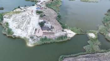 An aerial view of a riverside construction scene featuring sandy land and equipment along the water.