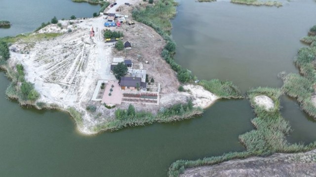 An aerial view of a riverside construction scene featuring sandy land and equipment along the water.