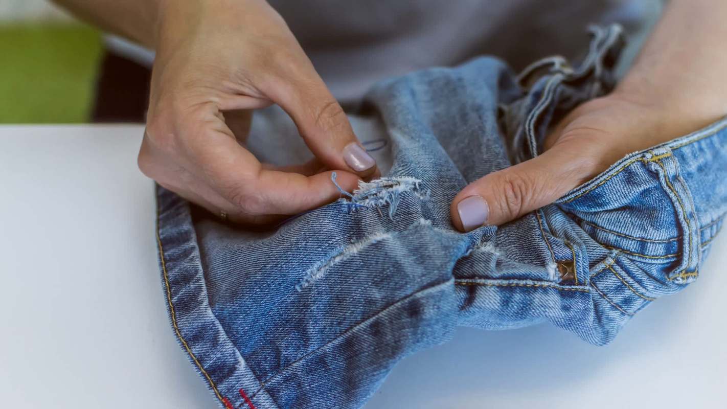 A person repairing a tear in a pair of denim jeans with their hands.