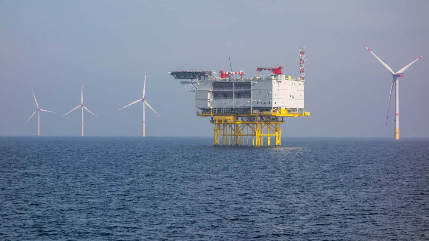 An offshore wind farm featuring a platform and several wind turbines against a misty sea backdrop.