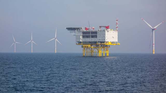 An offshore wind farm featuring a platform and several wind turbines against a misty sea backdrop.