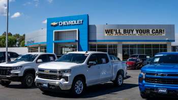A Chevrolet dealership displaying several trucks for sale, with a promotional sign saying "We'll buy your car!"