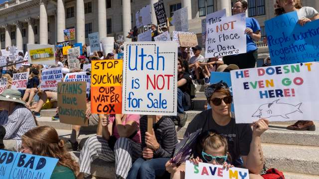 Protesters sit on steps holding signs against data centers and advocating for water conservation in Utah.