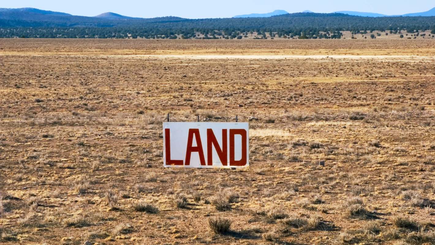 A large sign reading "LAND" stands in a sparse, dry landscape with distant mountains.