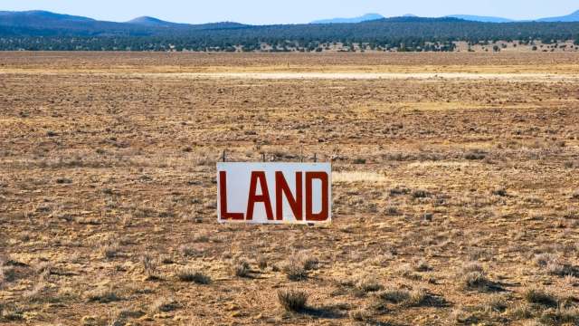 A large sign reading "LAND" stands in a sparse, dry landscape with distant mountains.