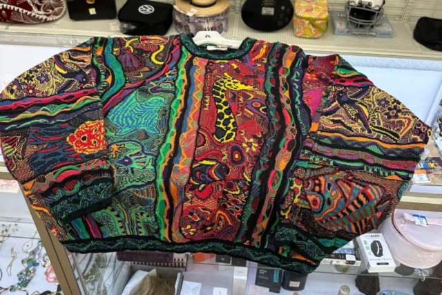 A colorful, patterned oversized sweater displayed on a hanger in a store.