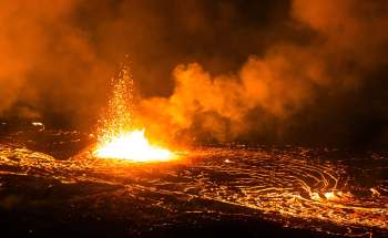 A lava eruption spewing bright flames and sparks against a backdrop of smoke and glowing molten rock.