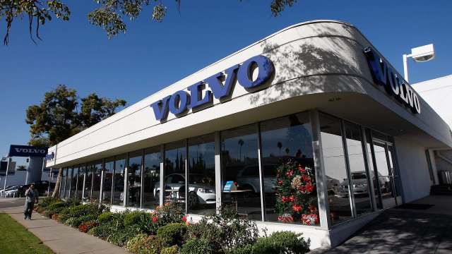A Volvo dealership with large windows, colorful flowers, and a clear blue sky in the background.