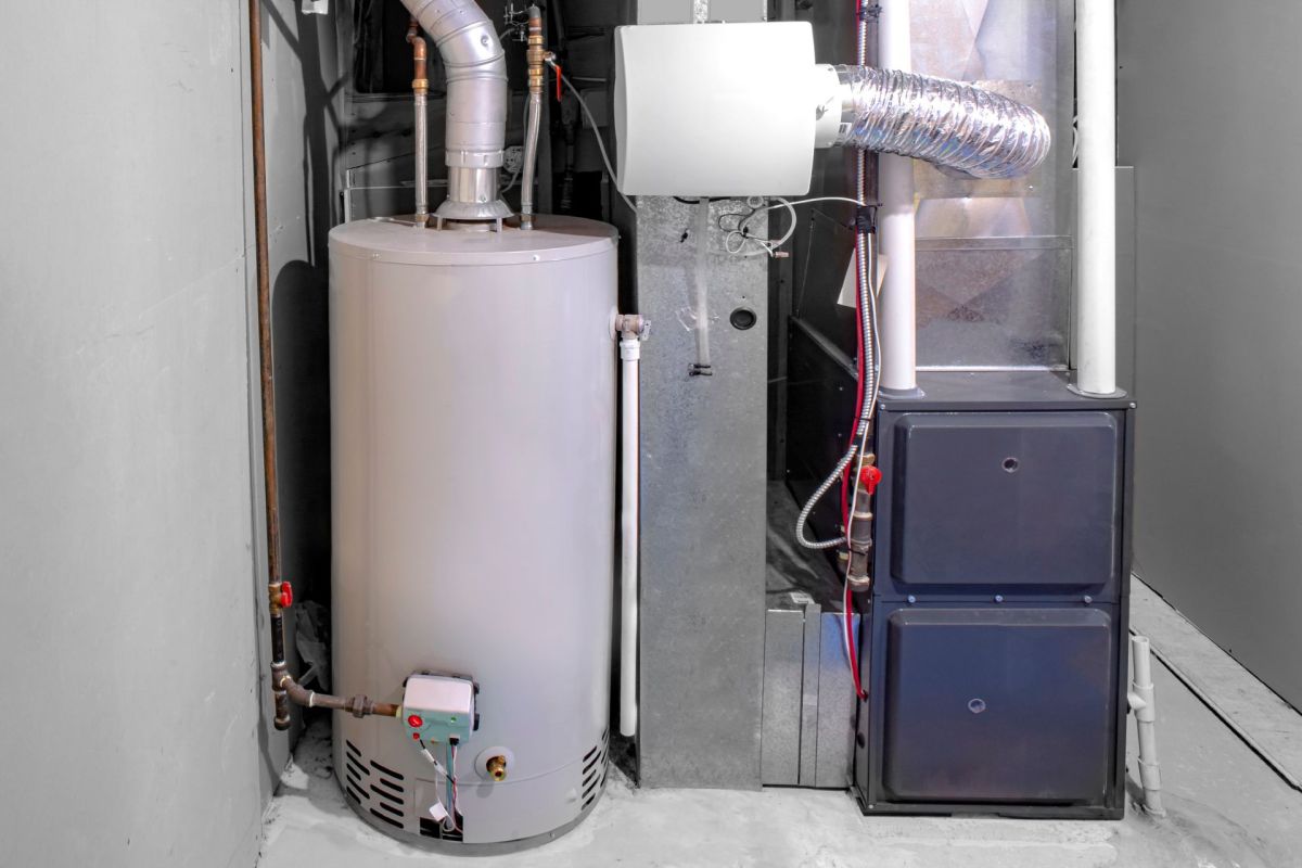A water heater and a furnace are situated in a basement utility room with gray walls.
