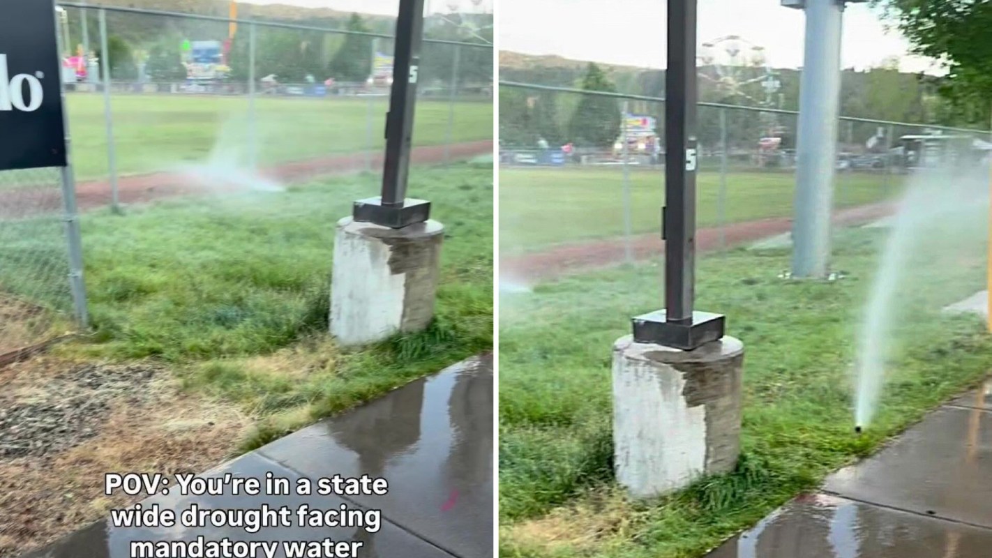 A view of a sports field with sprinklers running amidst dry grass, highlighting a water scarcity context.