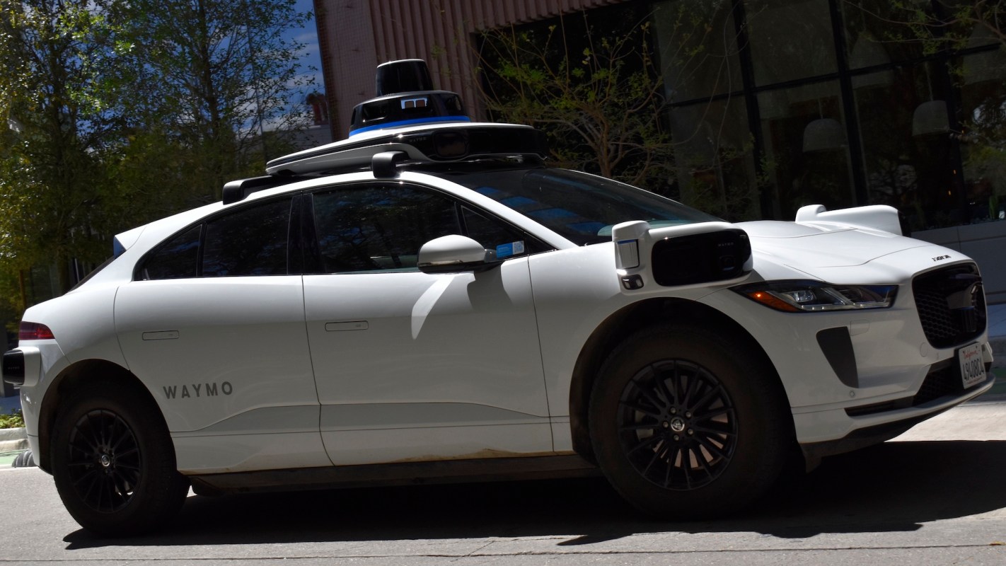 A white Waymo autonomous vehicle parked on a city street.