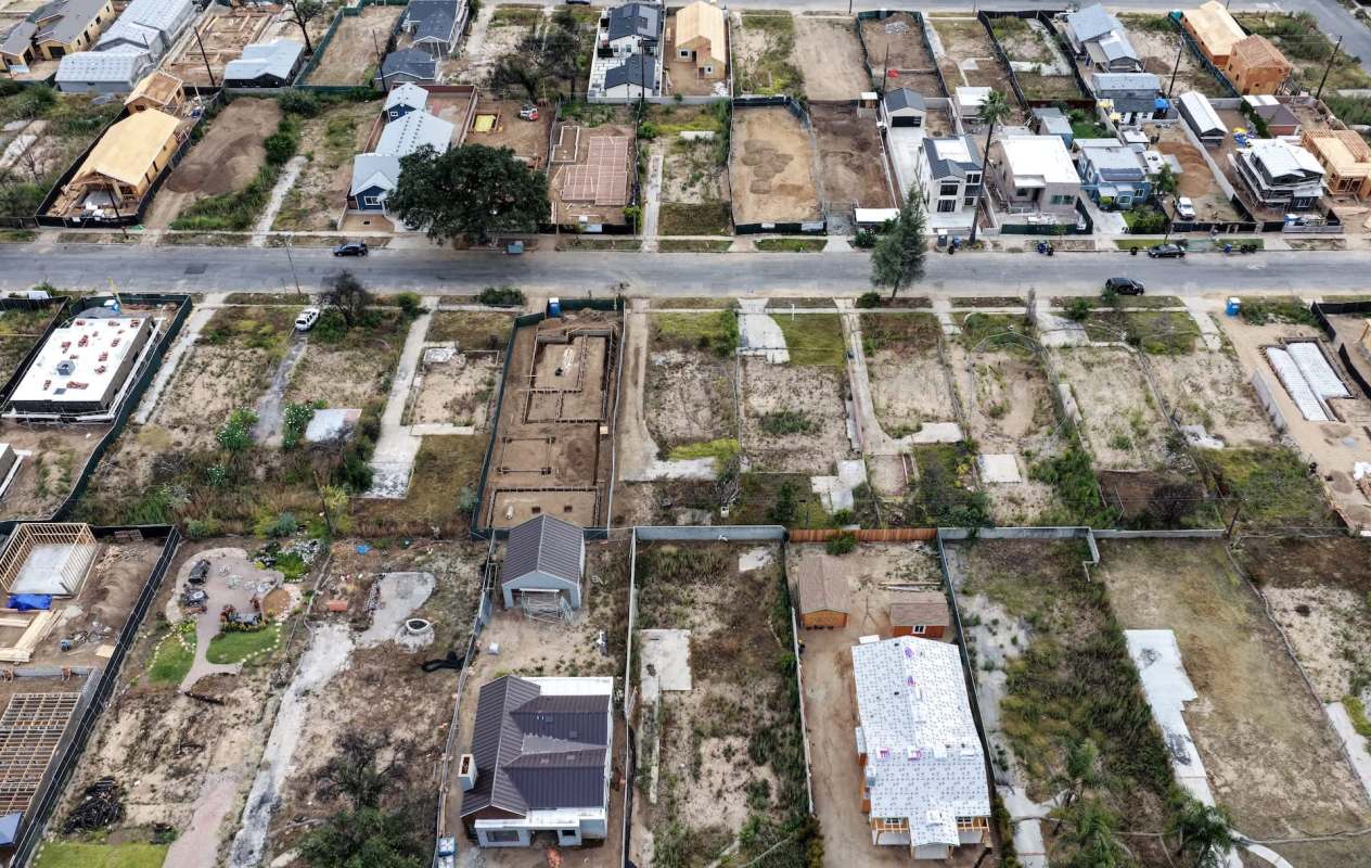 An aerial view of a construction site with several homes and empty lots in various stages of development after a wildfire.