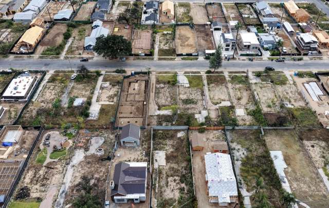 An aerial view of a construction site with several homes and empty lots in various stages of development after a wildfire.
