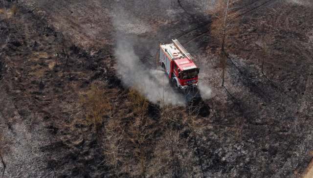 A fire truck drives through a charred landscape, with smoke rising from the affected area.