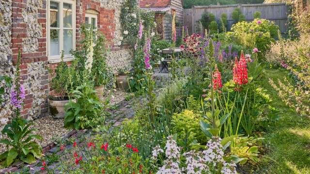 A lush English country garden filled with colorful flowers and plants alongside a brick wall and a small seating area.