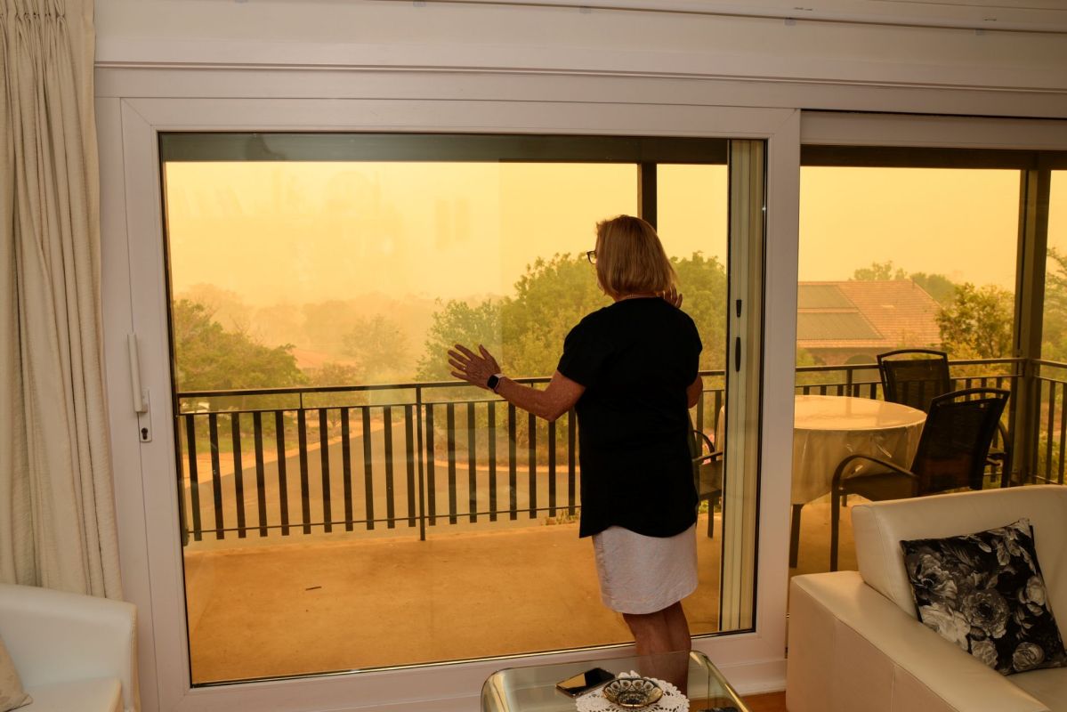 A person looks out at a hazy sky through a large glass door.