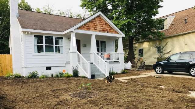 A renovated white cottage with a porch and a dog playing on freshly prepared landscaping.