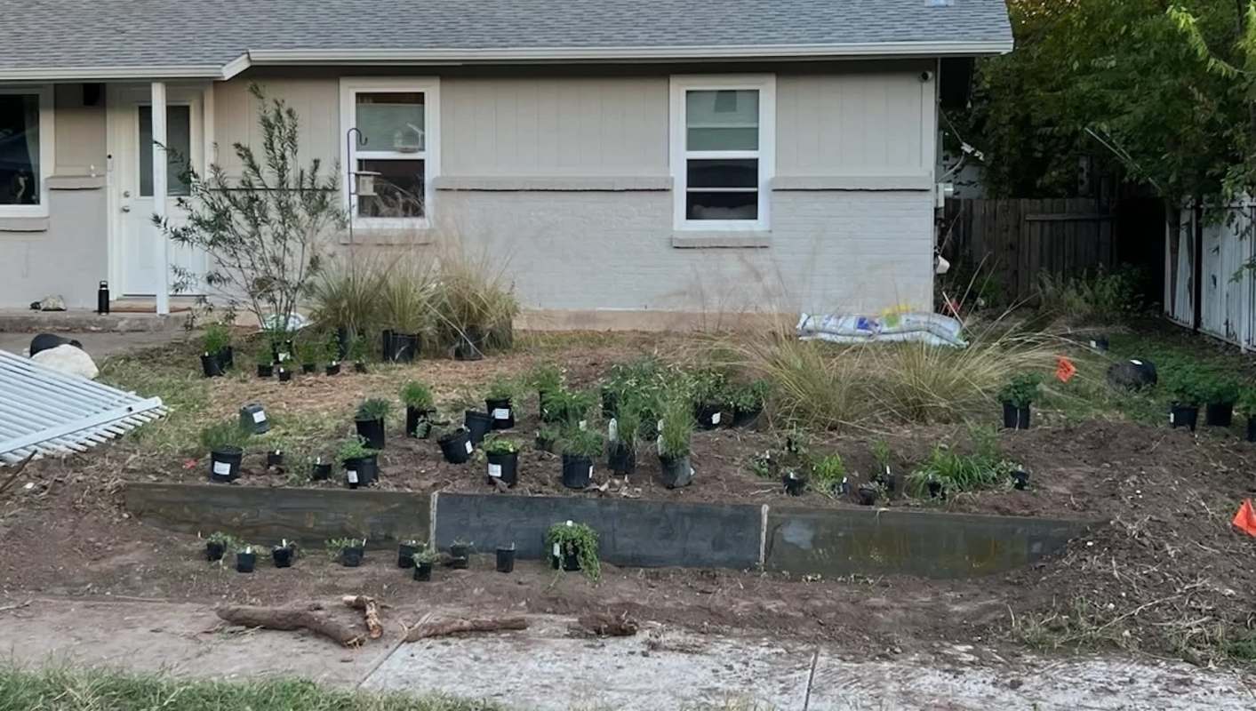 A garden bed with potted plants and a partially constructed flowerbed outside a house.