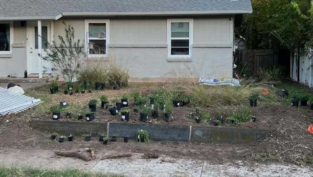 A garden bed with potted plants and a partially constructed flowerbed outside a house.