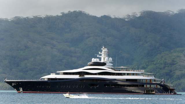 A large luxury yacht anchored near a lush, green hillside with a small speedboat nearby.