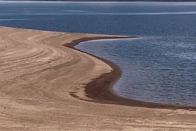 A sandy shoreline curves gently along the edge of a calm blue body of water.