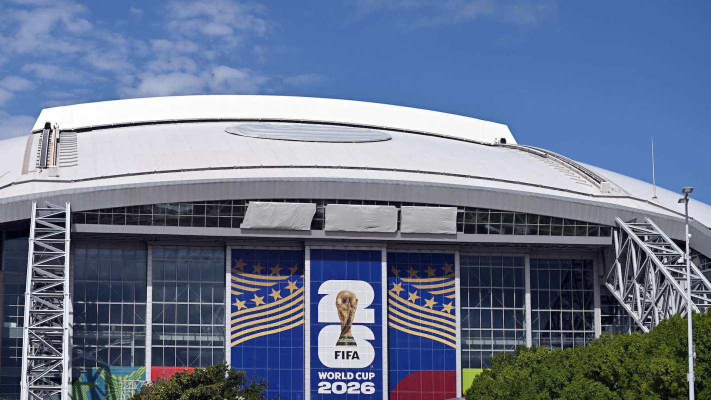 A modern stadium facade displaying the FIFA World Cup 2026 logo against a clear blue sky.