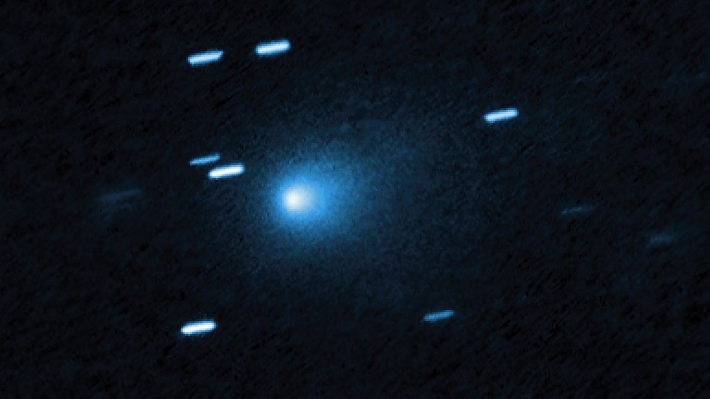 A bright blue comet surrounded by faint trails of light against a dark background.