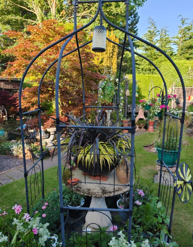 An iron gazebo over a stone table with a potted plant. 
