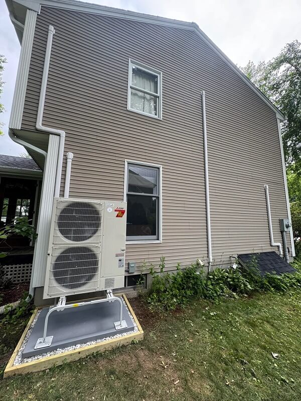An outdoor air conditioning unit is installed next to a home's beige siding, with a window visible above it.