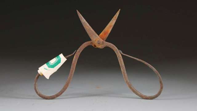 An antique pair of rusted scissors with a paper label, placed against a dark background.
