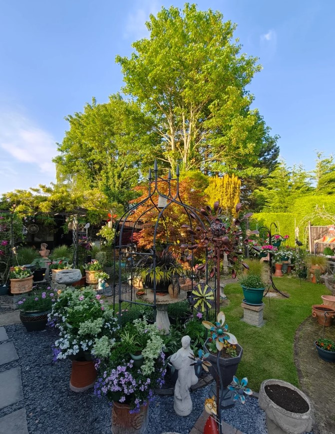 A whimsical garden featuring an iron gazebo, sculptures, colorful flowers, and green hedges. 