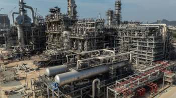 Construction of an extensive oil refinery with complex piping and structures under a clear sky.