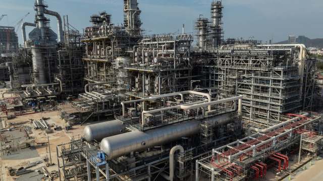 Construction of an extensive oil refinery with complex piping and structures under a clear sky.