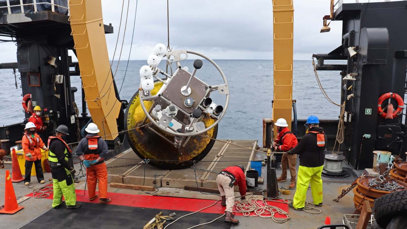 A research team on a ship brings aboard a research buoy from the ocean.