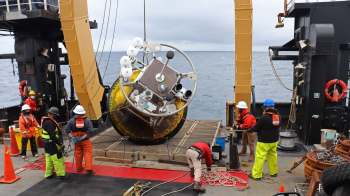 A research team on a ship brings aboard a research buoy from the ocean.