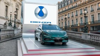 A green Denza Z9 GT car displayed on a platform with a logo backdrop in an urban setting.