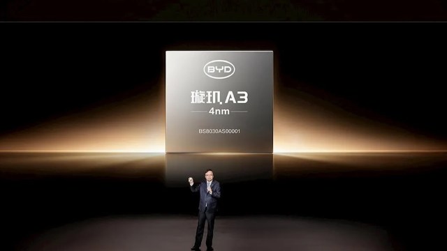 A presenter stands on stage next to a large screen displaying a BYD chip labeled "A3 4nm."