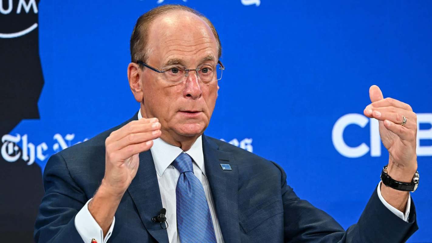 Larry Fink gestures with his hands while speaking at a forum, against a blue background with logos.