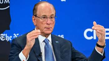 Larry Fink gestures with his hands while speaking at a forum, against a blue background with logos.