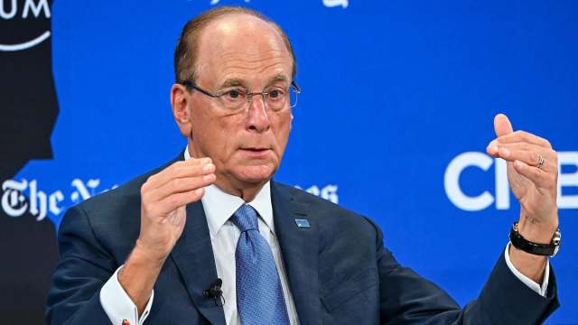 Larry Fink gestures with his hands while speaking at a forum, against a blue background with logos.