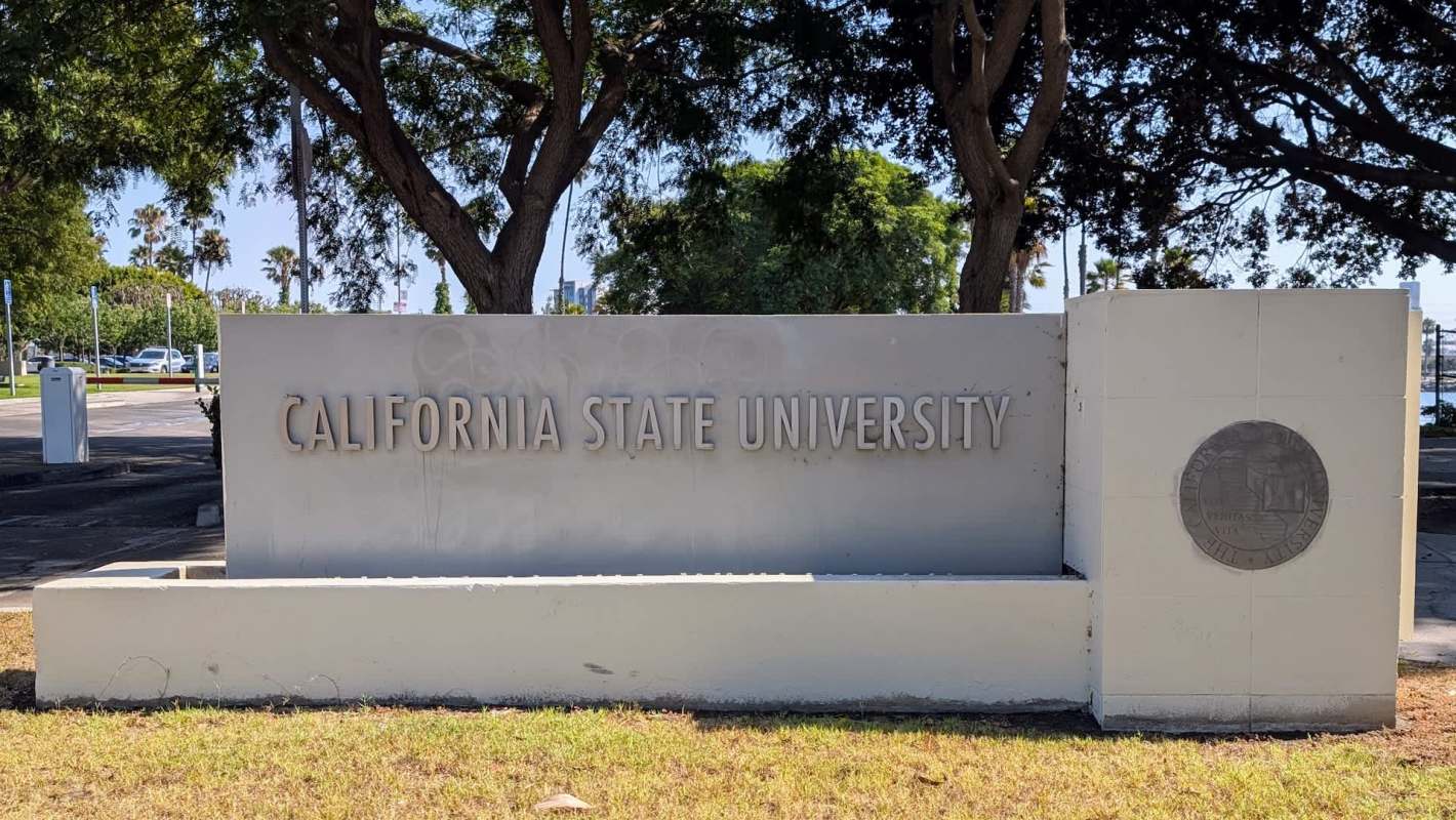 A sign for California State University surrounded by trees and greenery.