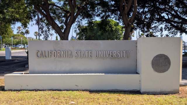 A sign for California State University surrounded by trees and greenery.