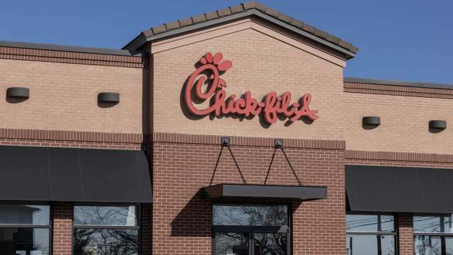 A close-up of a Chick-fil-A restaurant exterior with a red logo against a tan brick background.