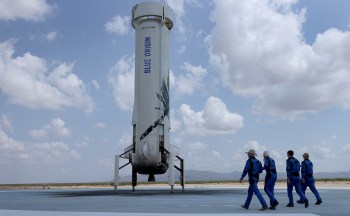 Four crew members walk toward a Blue Origin rocket on a launch pad.