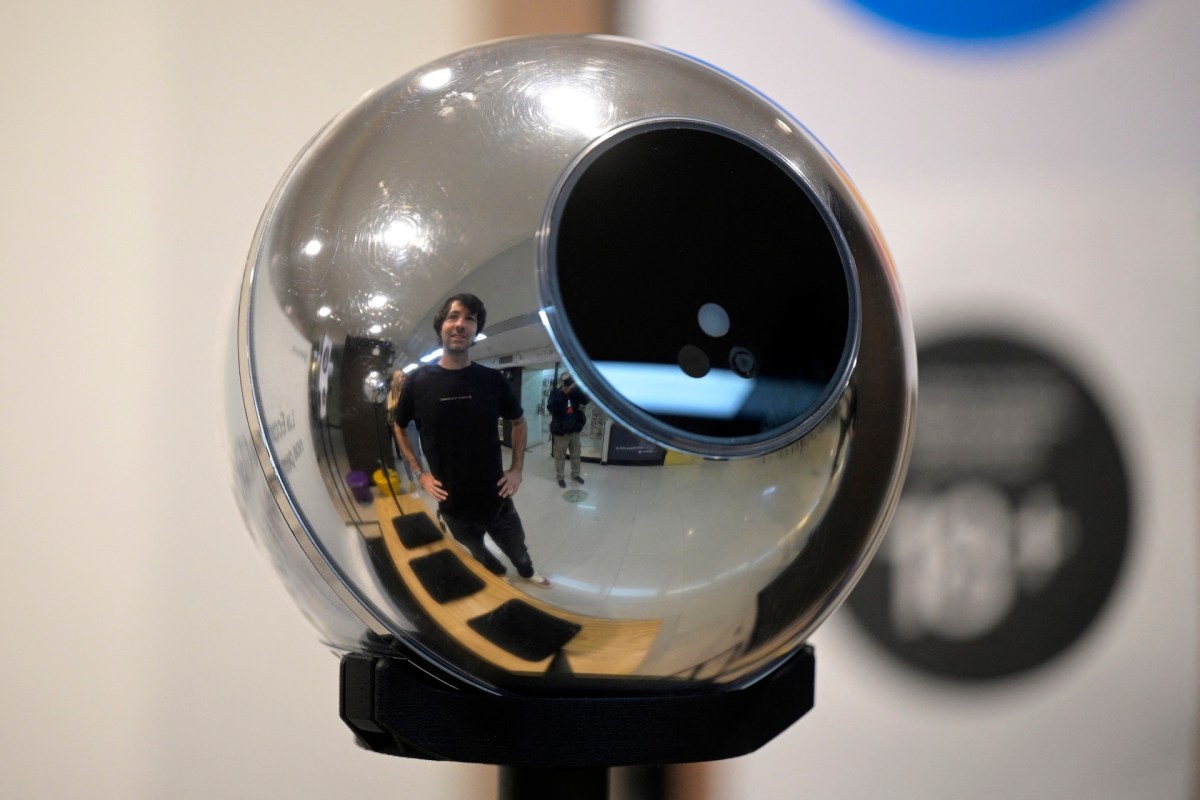 A reflective spherical device displays a man standing nearby, surrounded by an indoor environment.