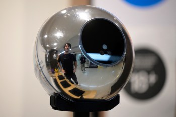 A reflective spherical device displays a man standing nearby, surrounded by an indoor environment.